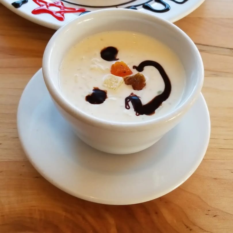 A white bowl of Indian rice pudding, garnished with chocolate syrup, dried fruit, and nuts.