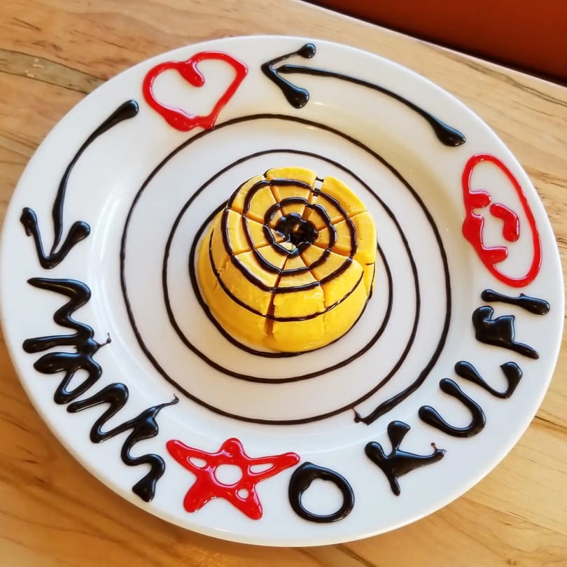 Mango Kulfi dessert with chocolate and red syrup decorations on a white plate.