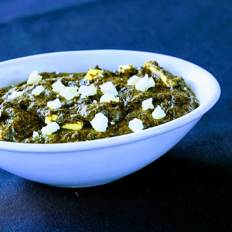 A white bowl filled with vibrant green palak paneer, topped with white paneer cubes.