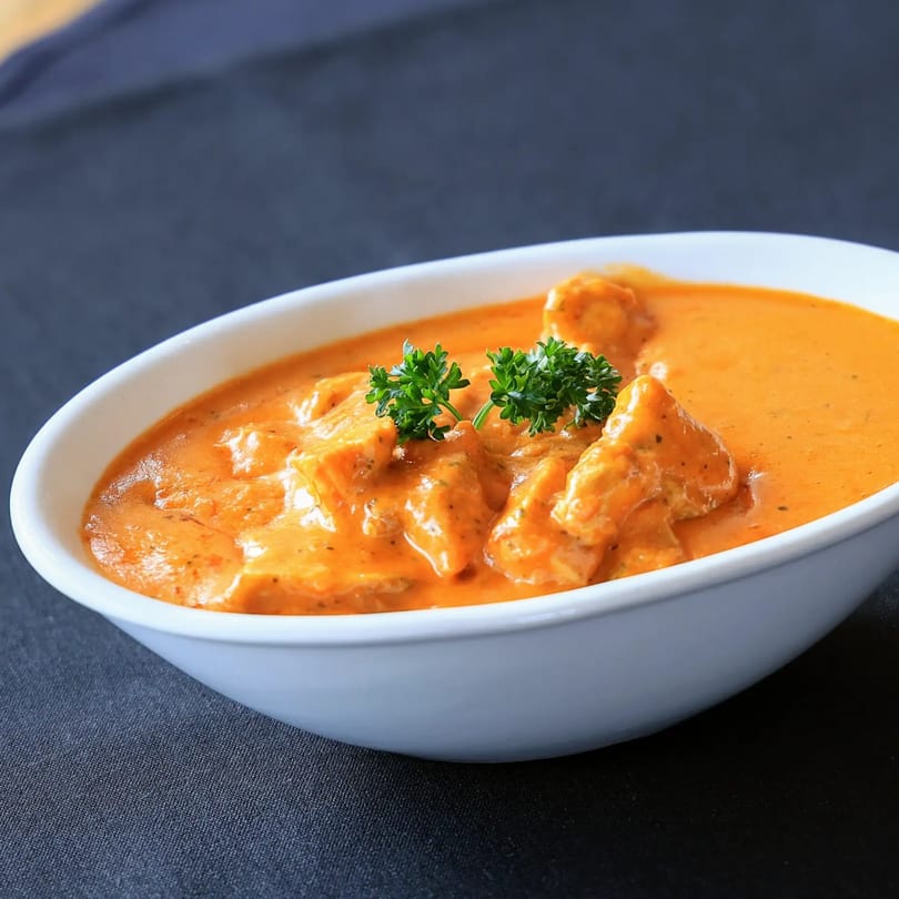 Zaika Indian Cuisine's butter chicken, a creamy orange curry with chicken pieces, garnished with parsley.