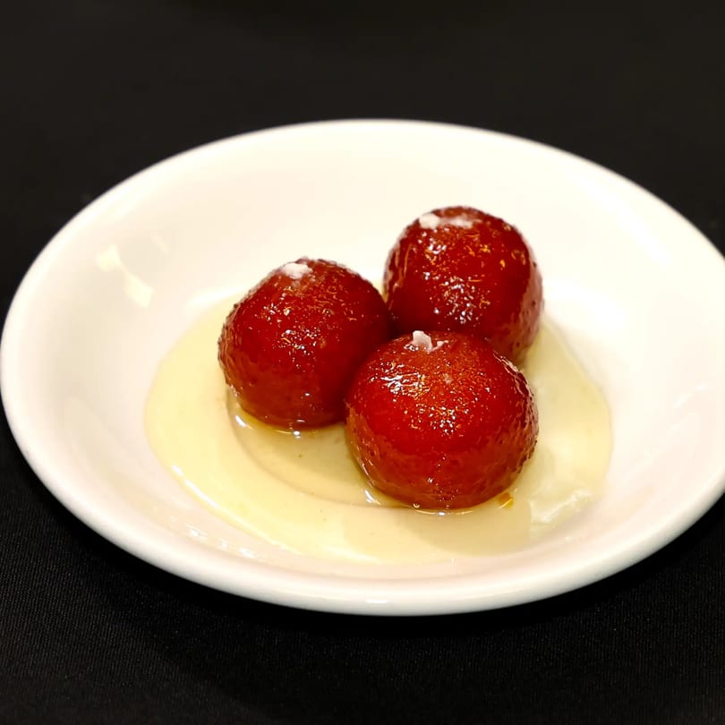 Three glistening gulab jamun, a traditional Indian dessert, served in a white bowl with syrup.