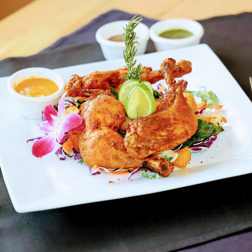 Zaika Indian Cuisine's Tandoori Chicken, garnished with lime, rosemary, and an orchid, served with sauces.